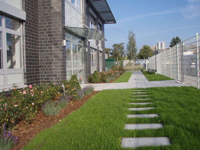 Der hochwertig gestaltete Zugangsbereich zum Empfang eines Fertigungs- und Serviceunternehmens muendet in einem Schrittplattenweg.